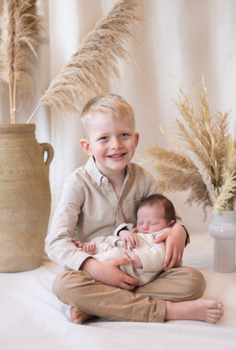 Young boy holding a baby with decorative plants and vases in the background during a family and child studio photoshoot near me