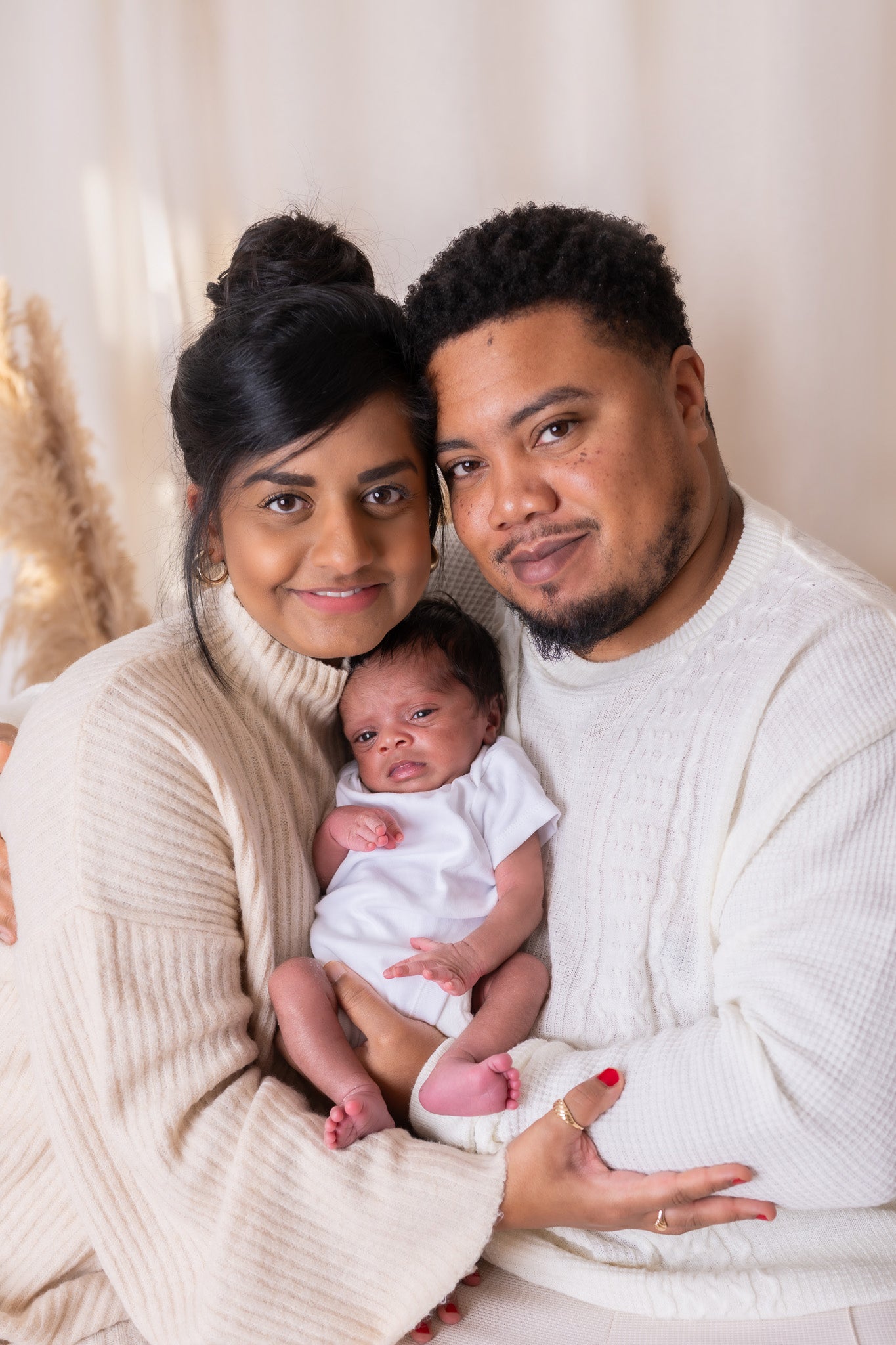 Family of three posing together with a baby in a neutral setting
