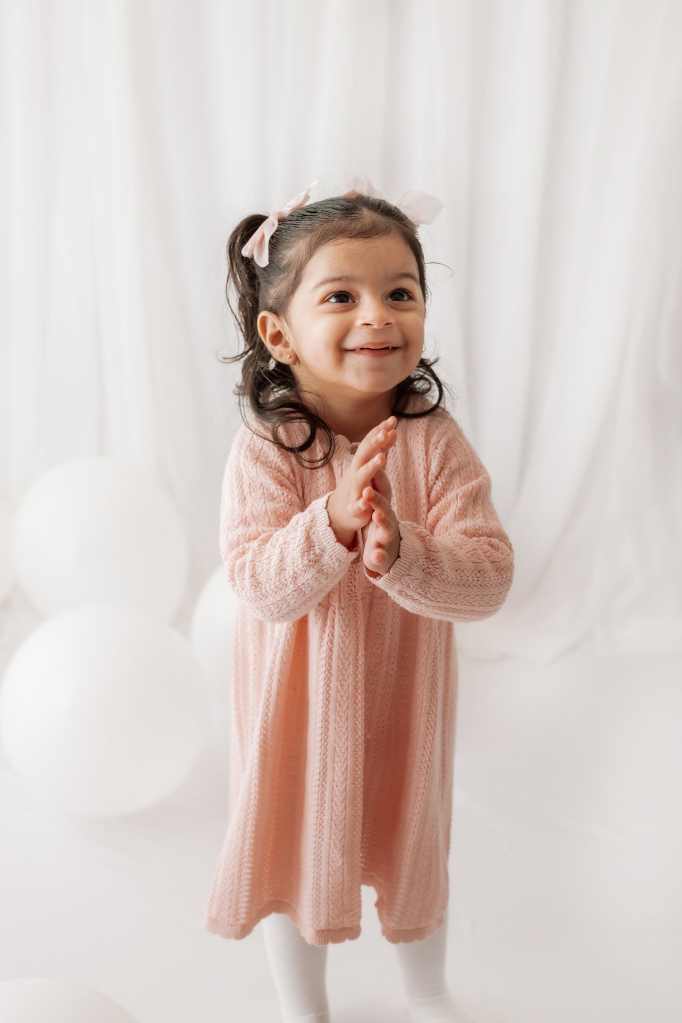 Young girl in a pink dress clapping hands against a white background