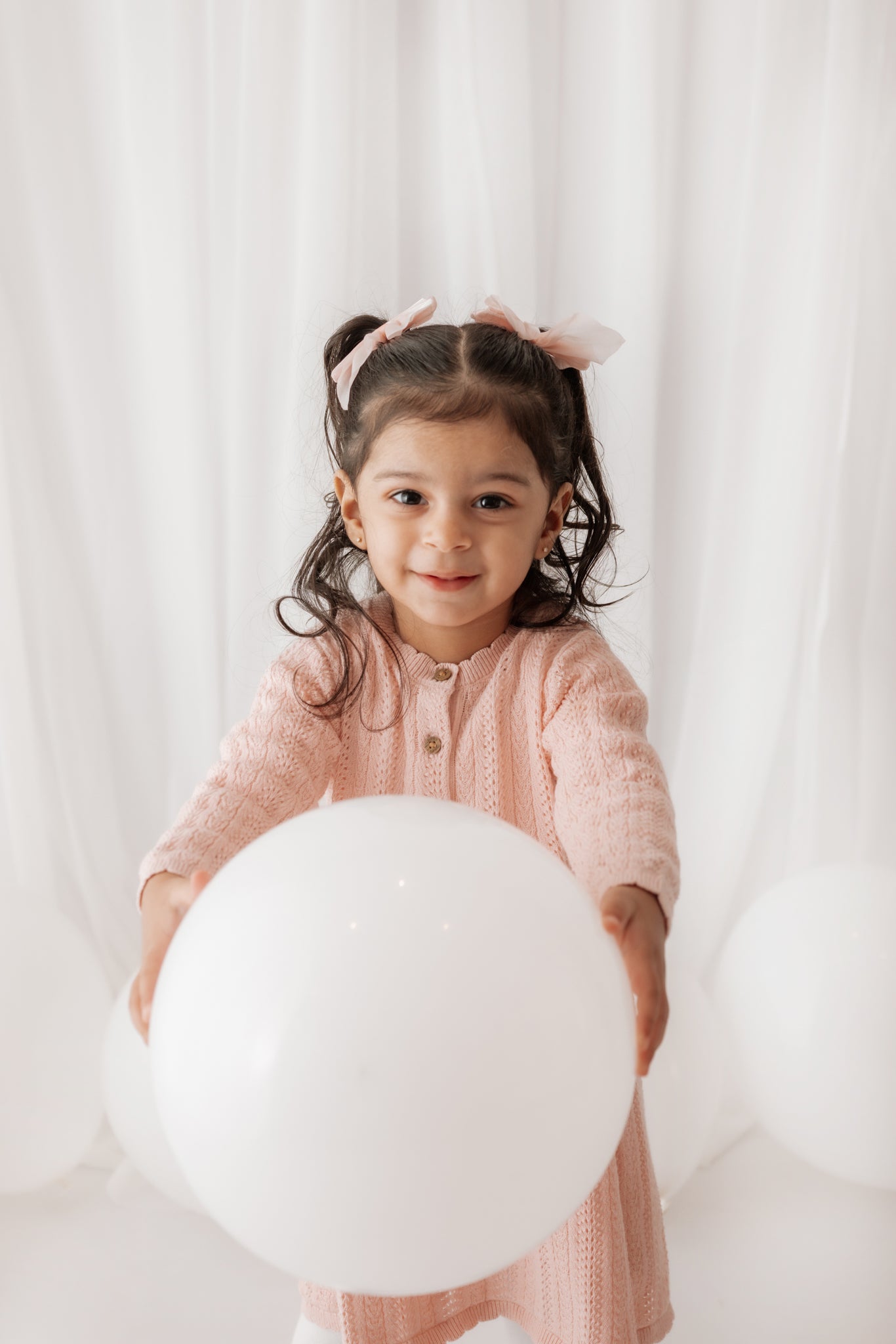 Child holding a large white balloon against a light curtain background in a photoshoot