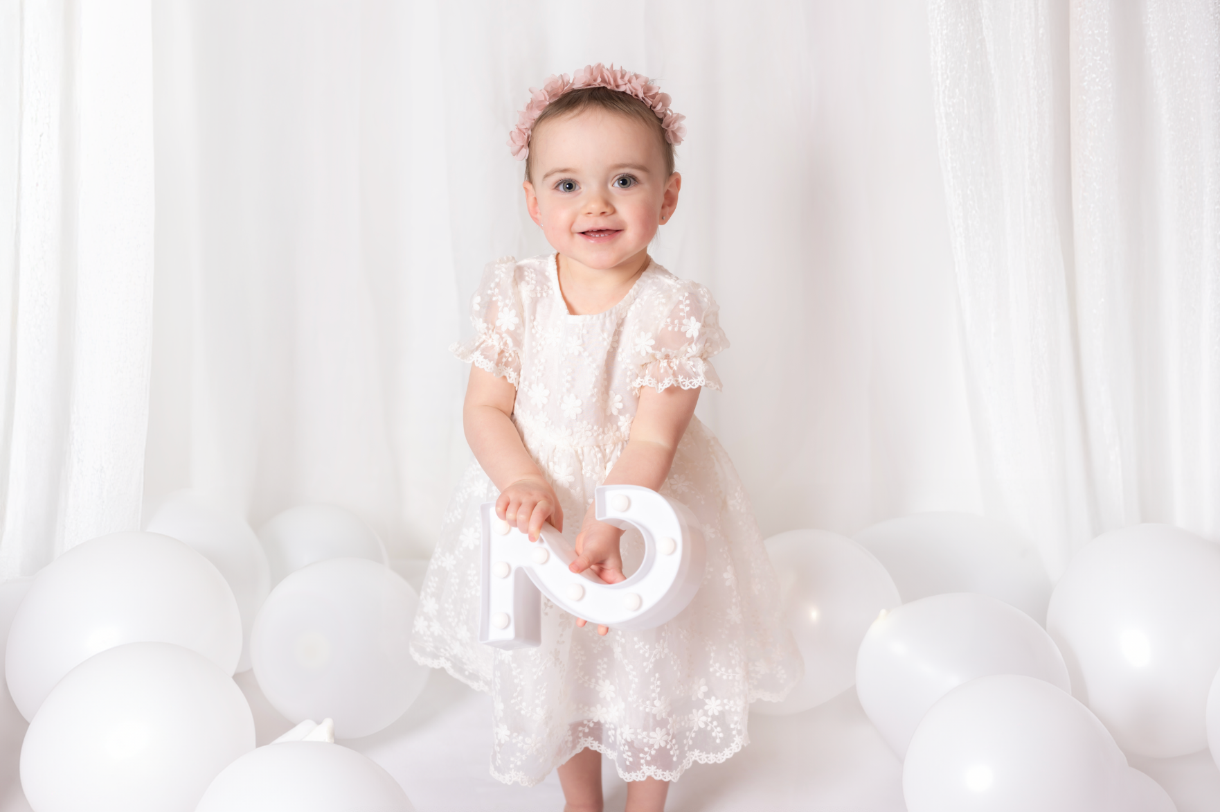 Baby in a white dress with floral details sitting on a white background