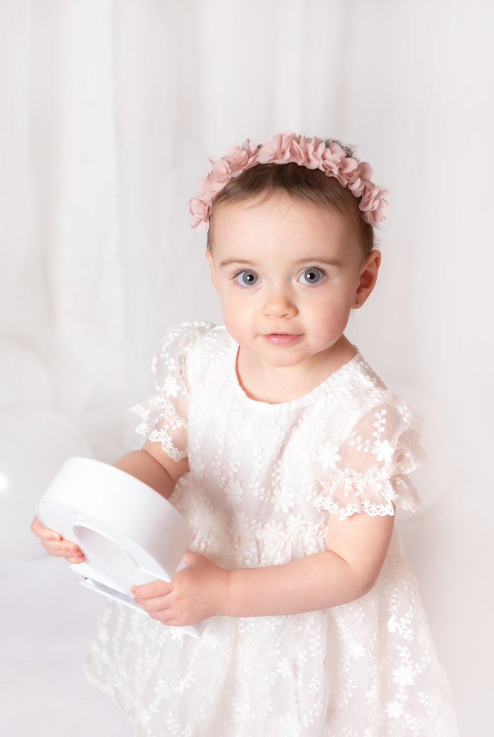 Young child in a white lace dress with a floral headband against a white background