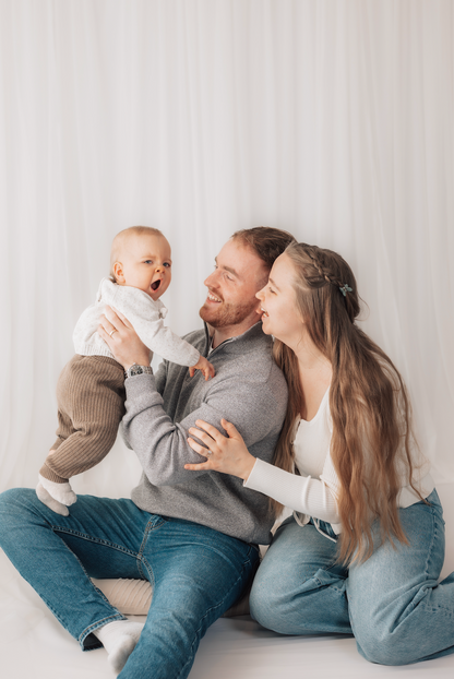 Family of three sitting together on a light-colored floor with a white wall background