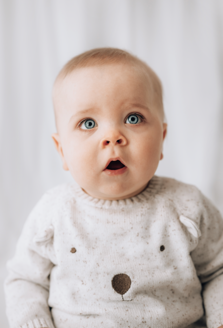 Baby wearing a white sweater with black buttons against a light background in photoshoot 