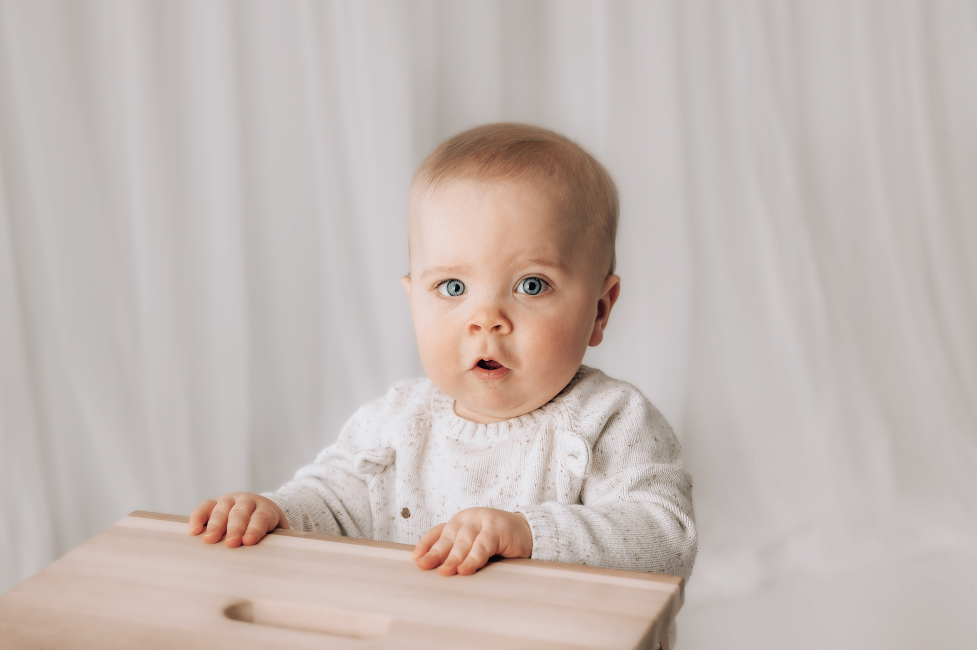 Baby sitting at a wooden table with a neutral background