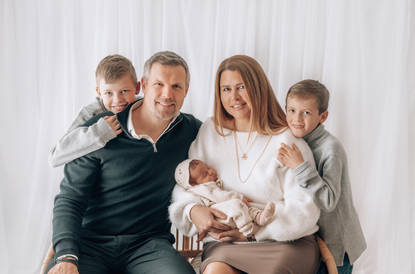Family of five with two adults and three children posing together on a white background during a newborn family photoshoot in Surrey