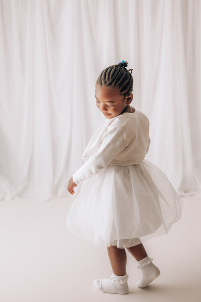 Young girl in a white dress standing against a white curtain