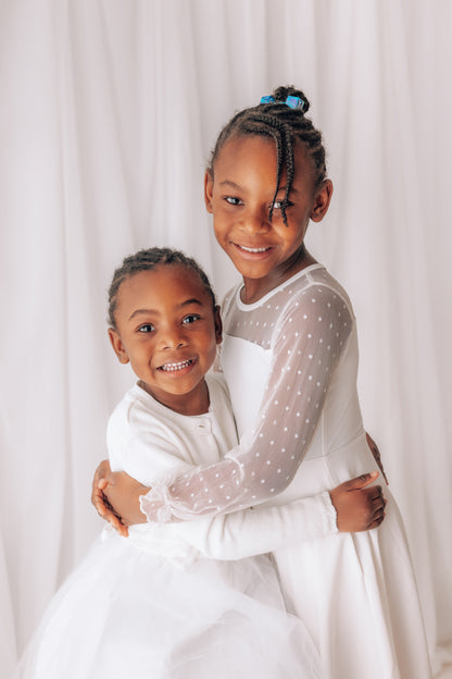Two children in white dresses hugging against a white background