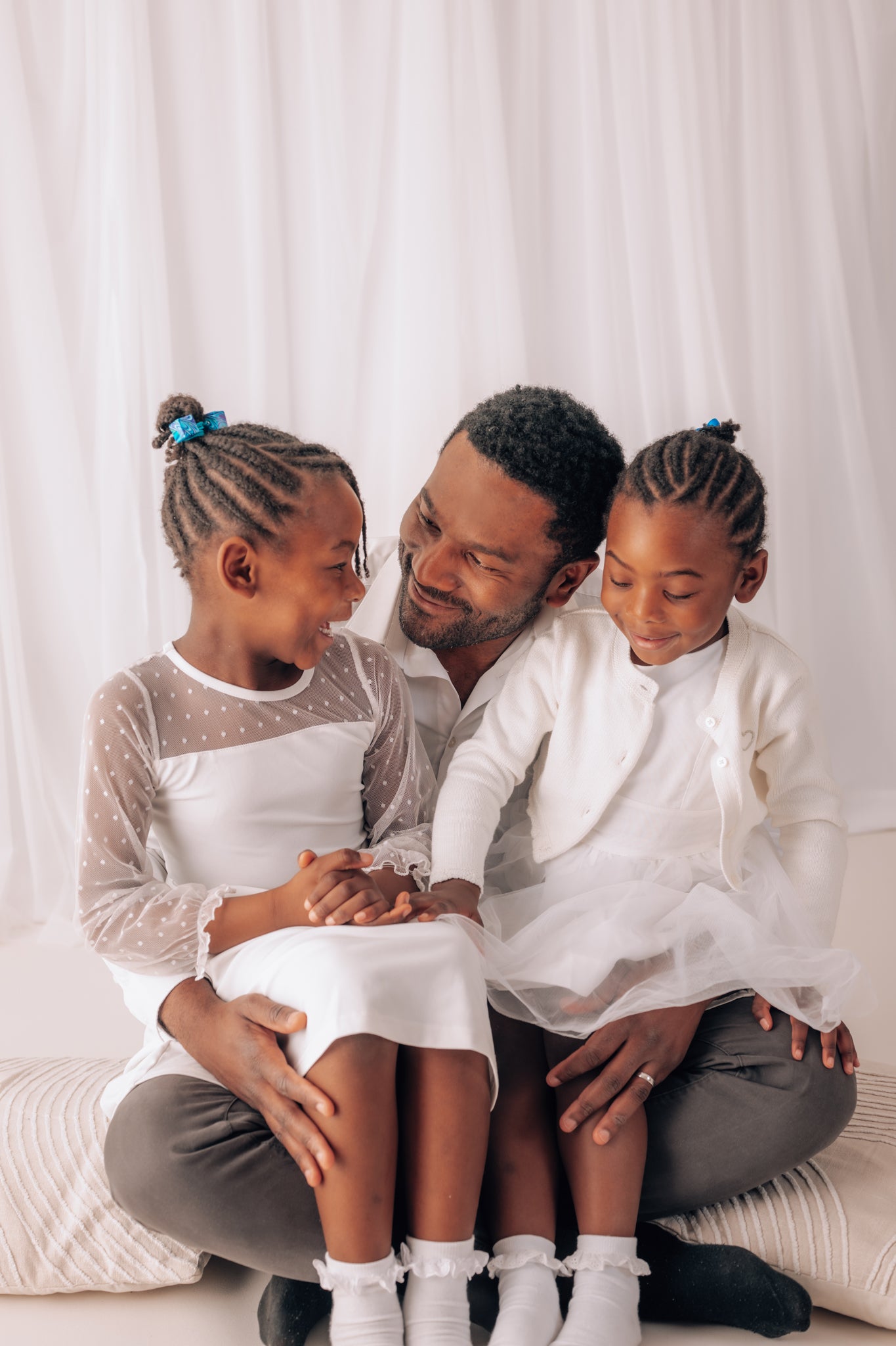 Man sitting with two young girls on a white couch against a white curtain background