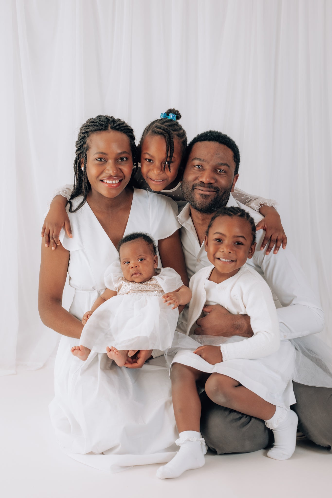 Family of five posing together in white clothing against a white background