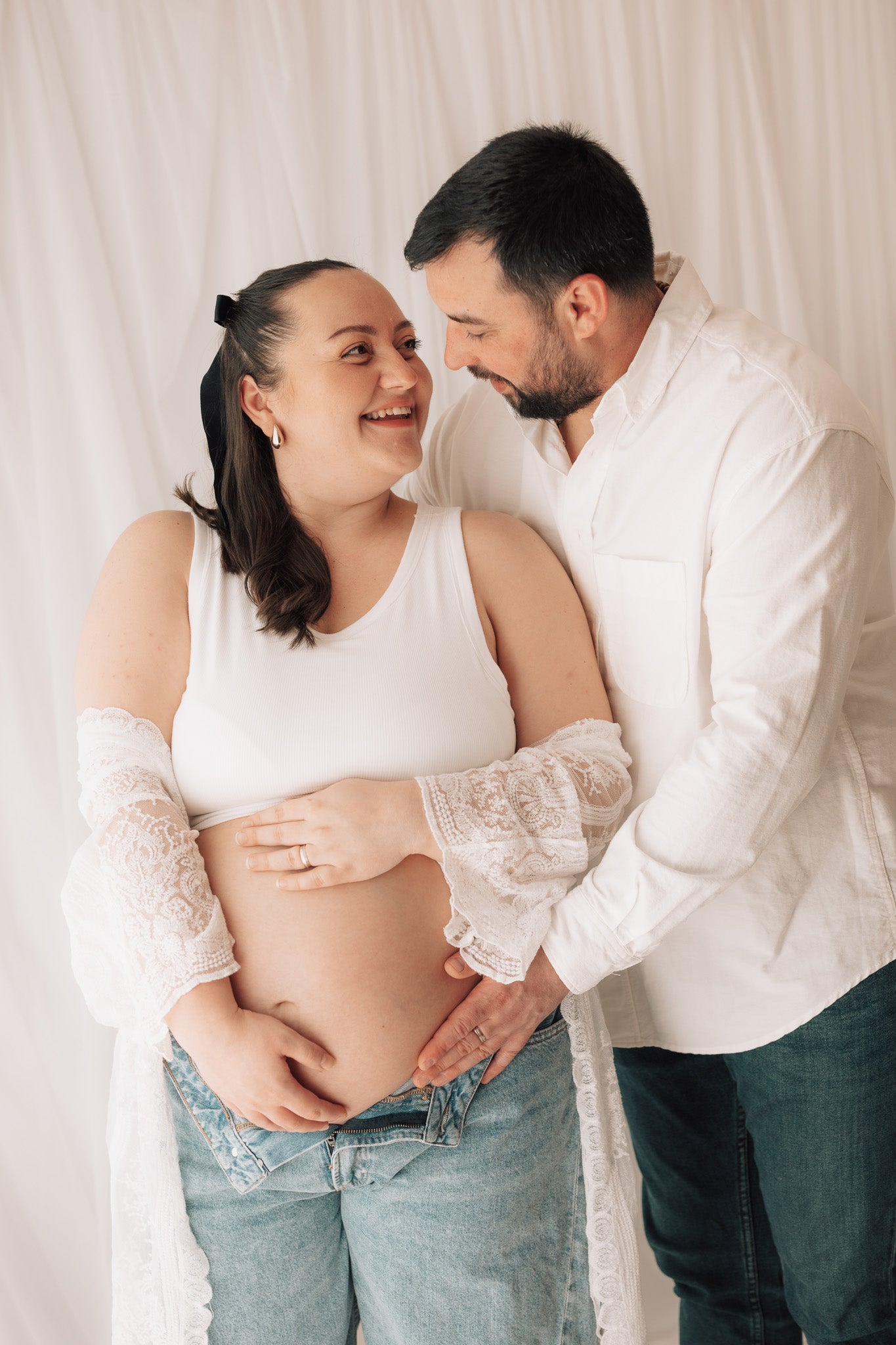 Pregnant woman with a man embracing her, both wearing white 