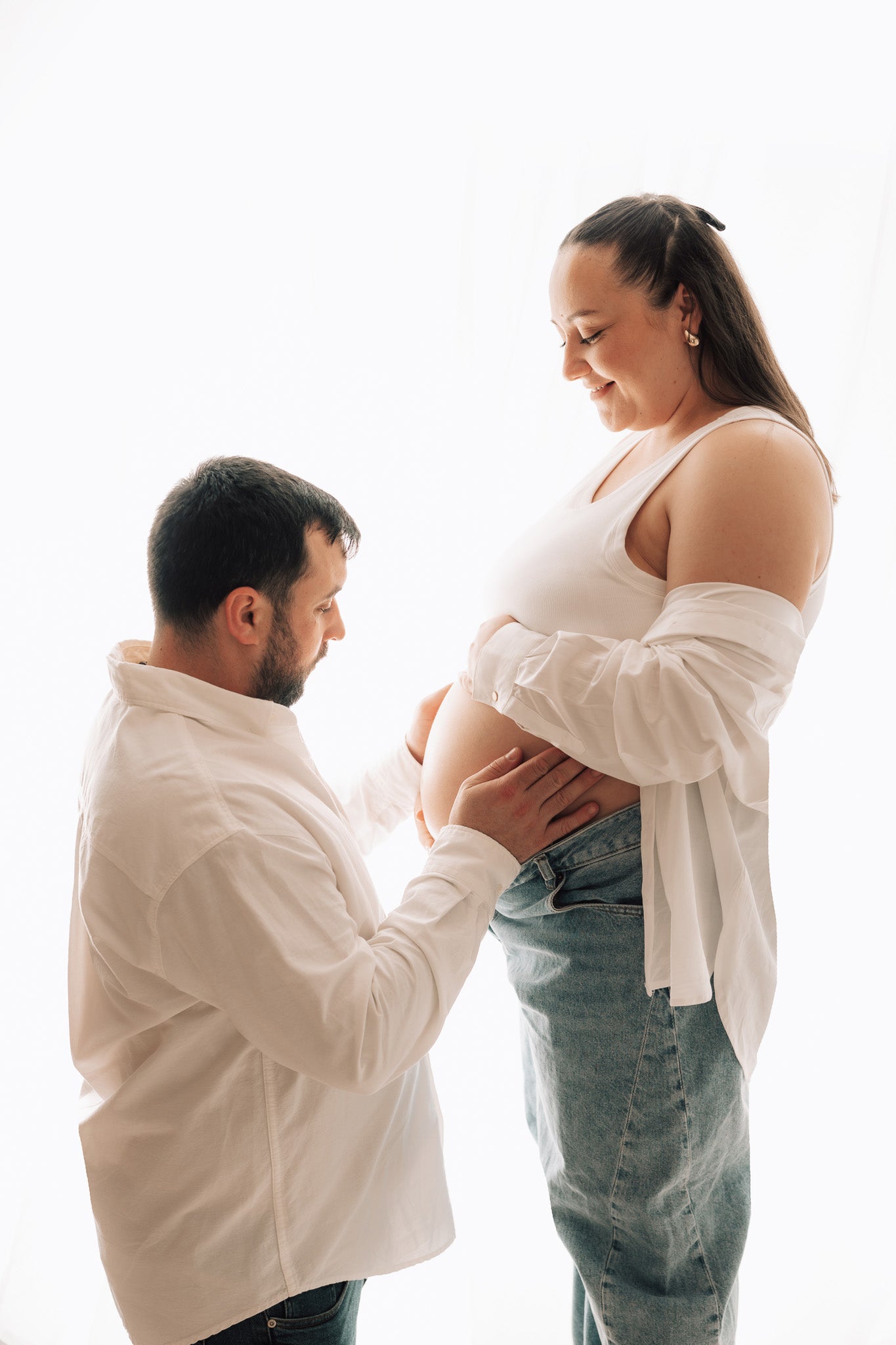 Man and woman standing close together, with the man gently holding the woman's pregnant belly.