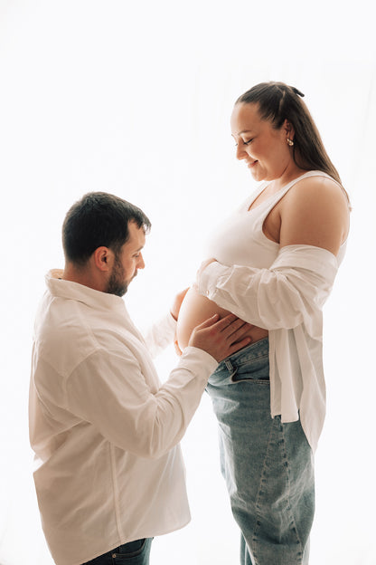 Man and woman standing close together, with the man gently holding the woman's pregnant belly.