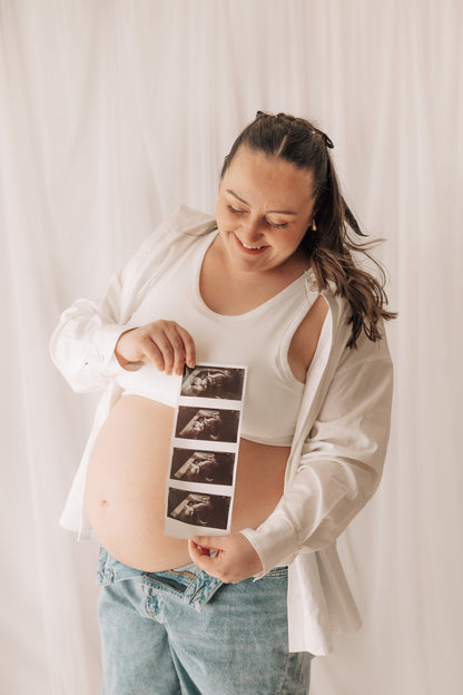 Pregnant woman holding ultrasound images against a white curtain
