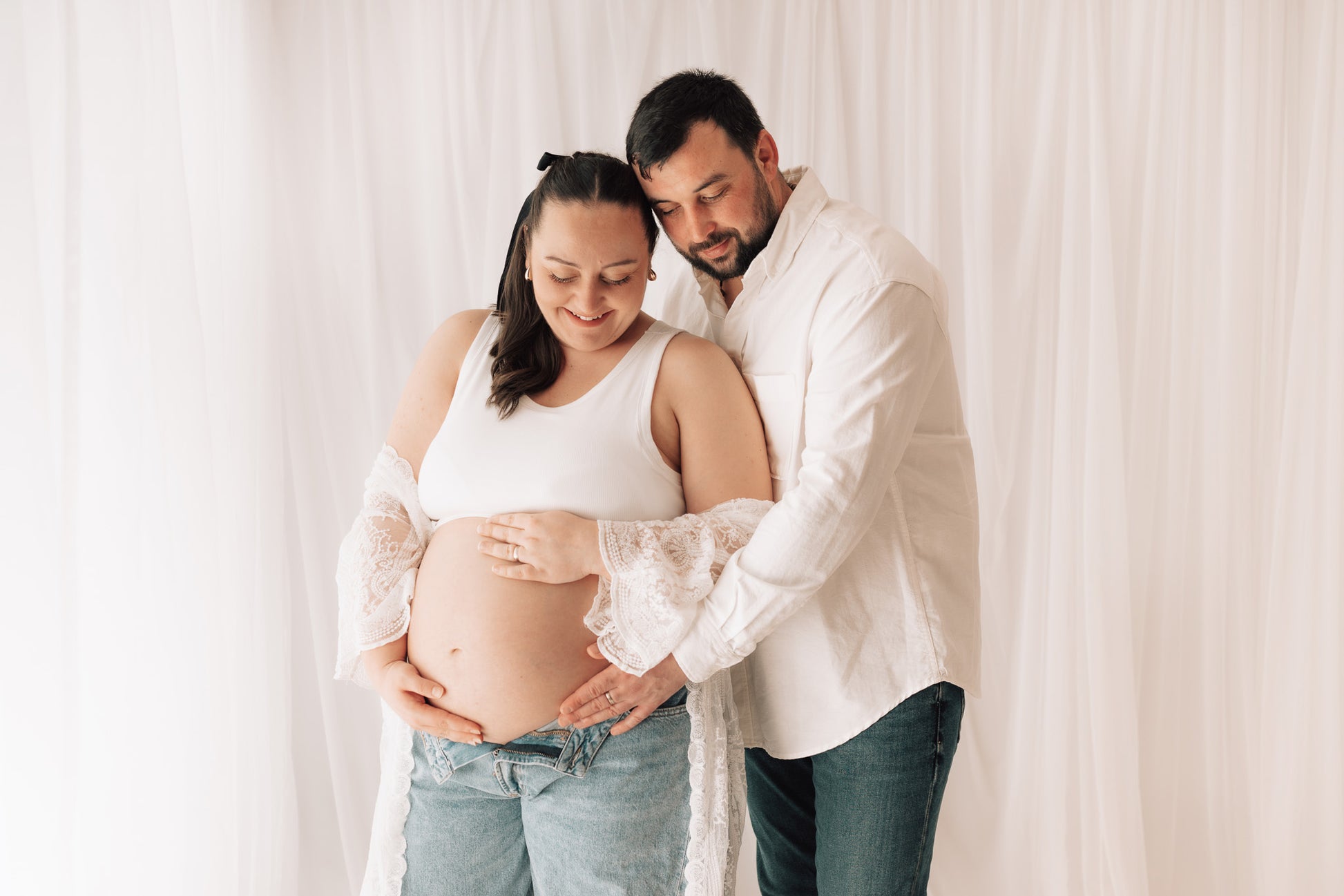 Pregnant woman and her partner posing together in a studio setting.