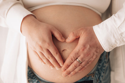Two hands forming a heart shape over a pregnant belly.