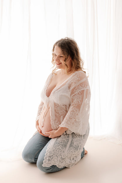 Pregnant woman wearing a lace robe in a softly lit room during a Surrey maternity and pregnancy photoshoot in studio