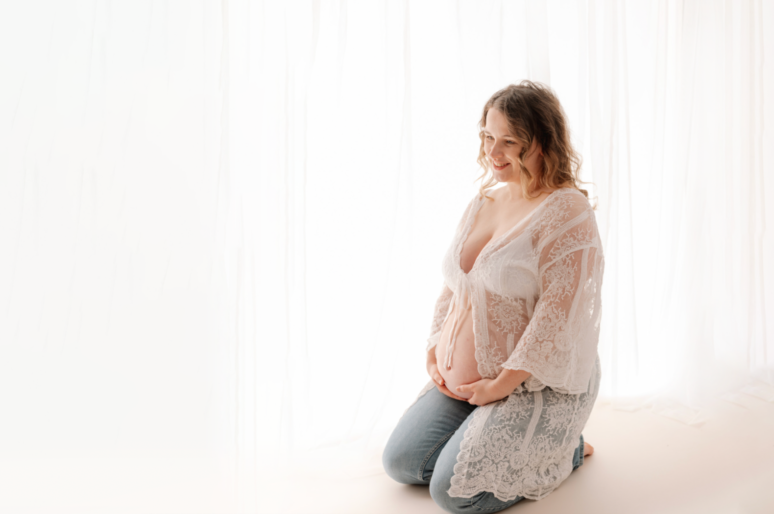 Pregnant woman sitting on a white floor with a light background