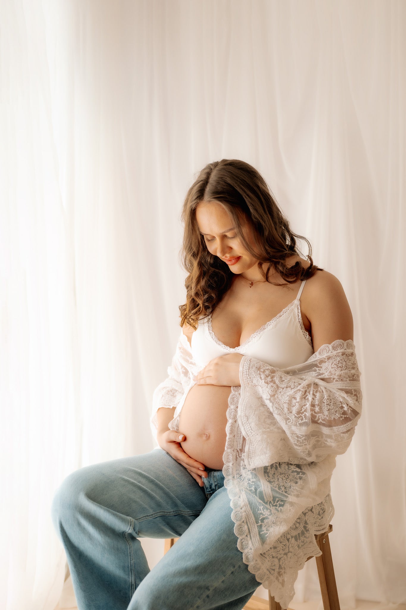 Pregnant woman sitting on a stool against a white curtain