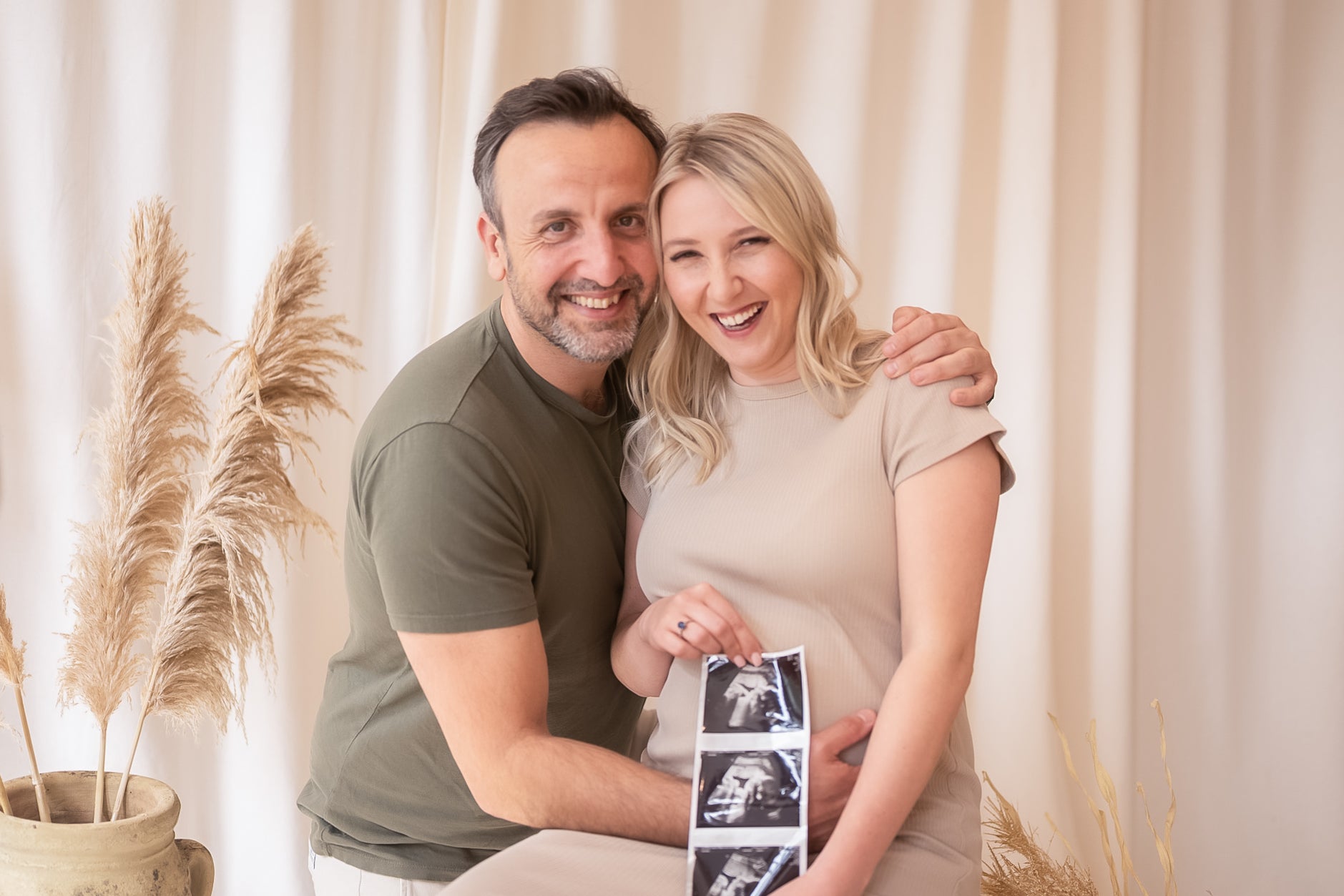 Pregnant woman holding ultrasound images with a man in a home setting.