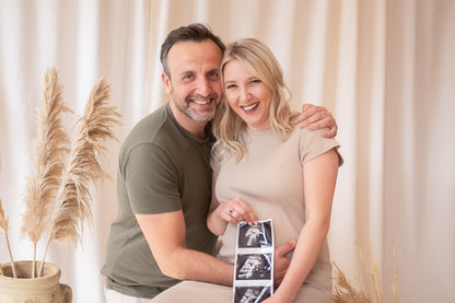 Pregnant woman holding ultrasound images with a man in a home setting.
