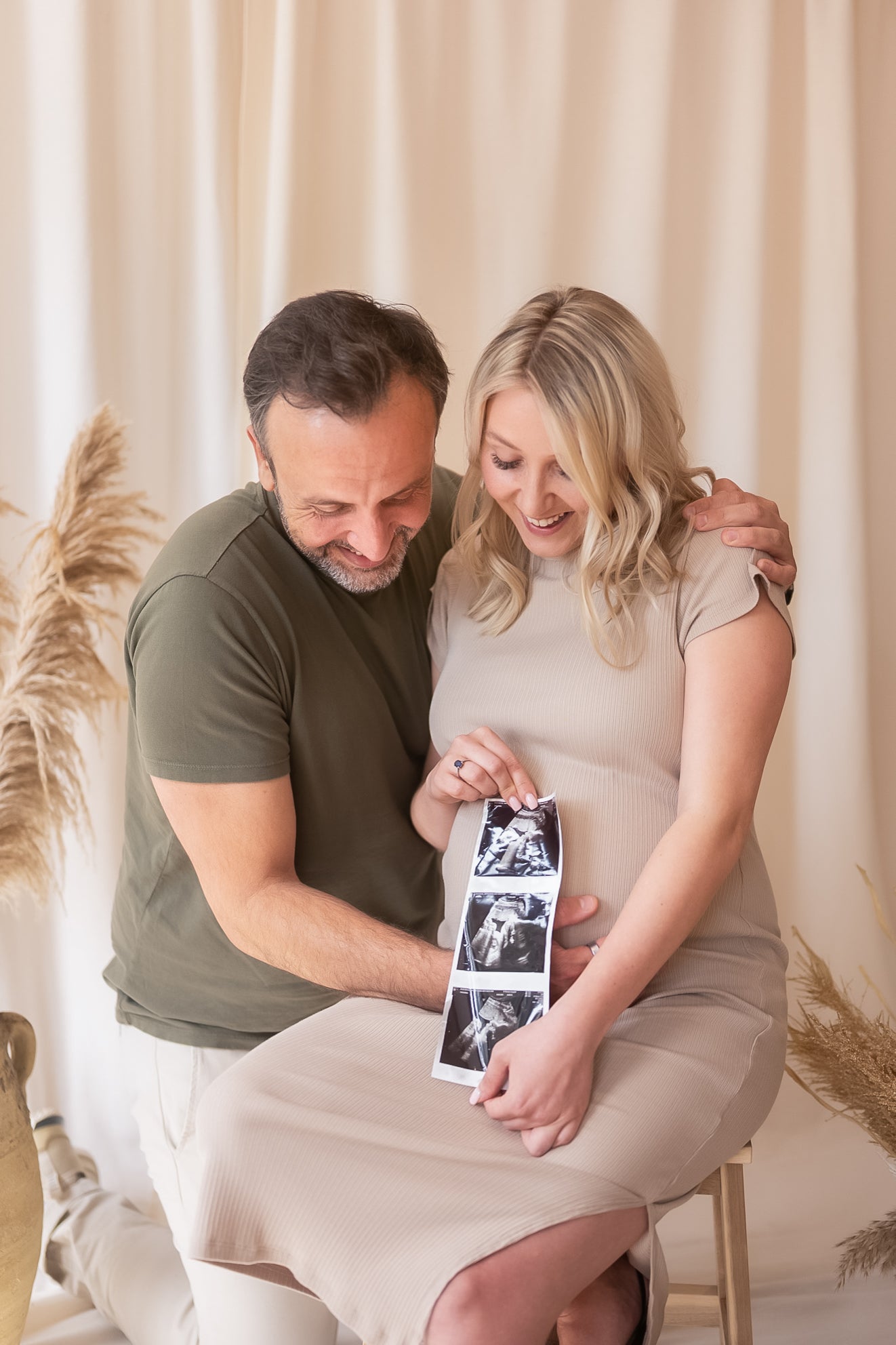 Pregnant woman holding ultrasound images with a man in a neutral setting