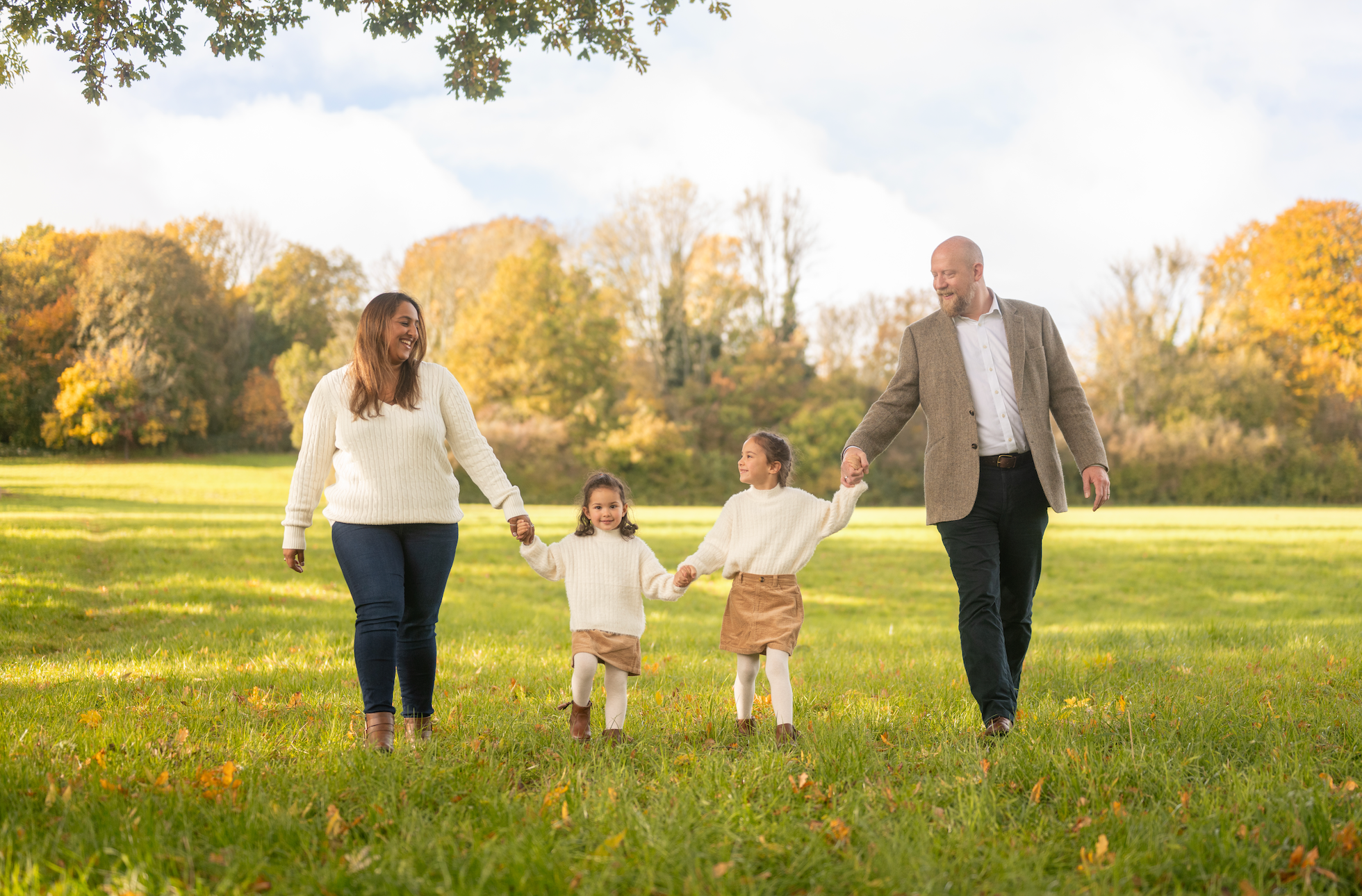Family of four walking together in a park with trees and grass in the background