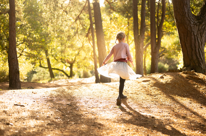 Person in a white dress walking on a dirt path in a sunlit forest