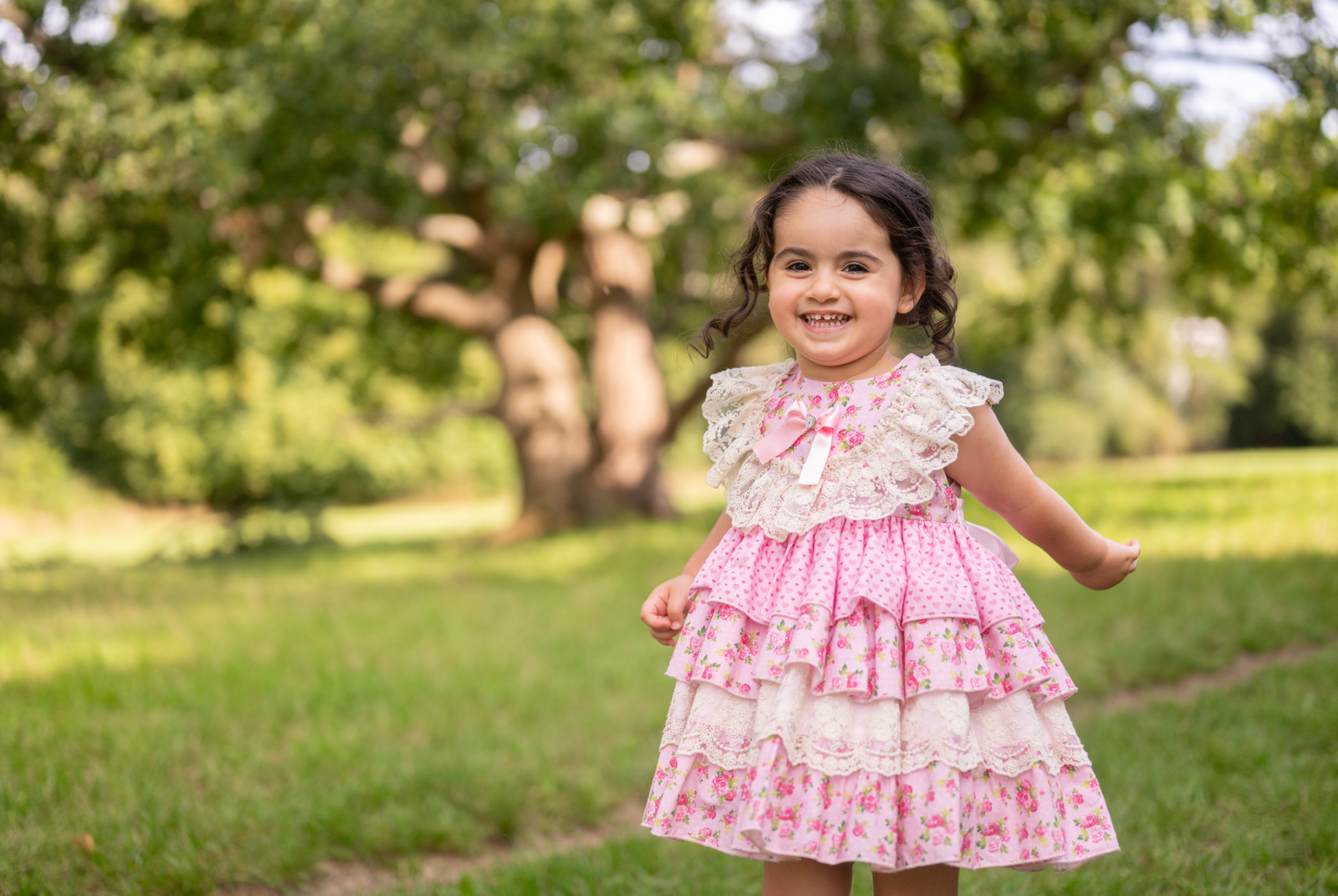 Young girl in a pink floral dress standing in a park with trees in the background